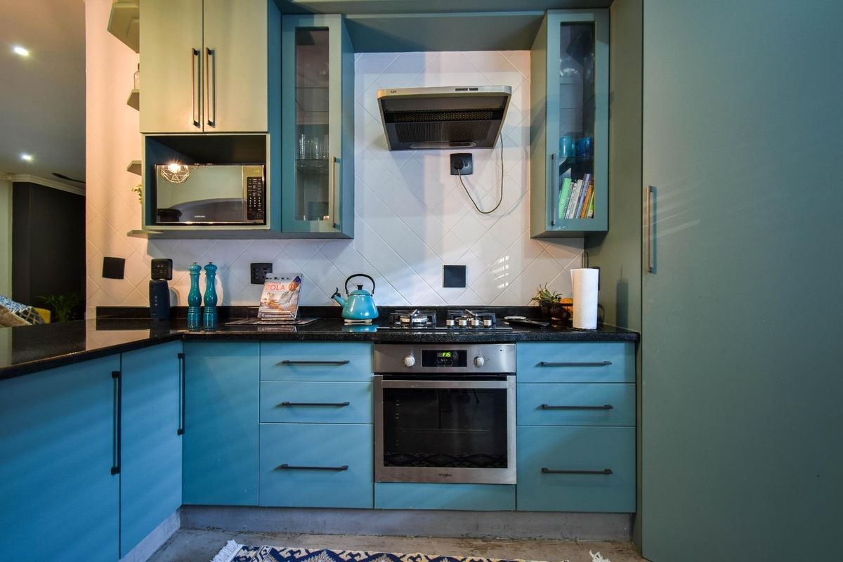 A modern kitchen featuring teal cabinetry, black granite countertops, a built-in oven, gas hob, and a stainless steel extractor fan.