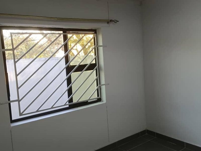 A clean, empty bedroom featuring tiled flooring, a window with security burglar bars, and a curtain rod installed.