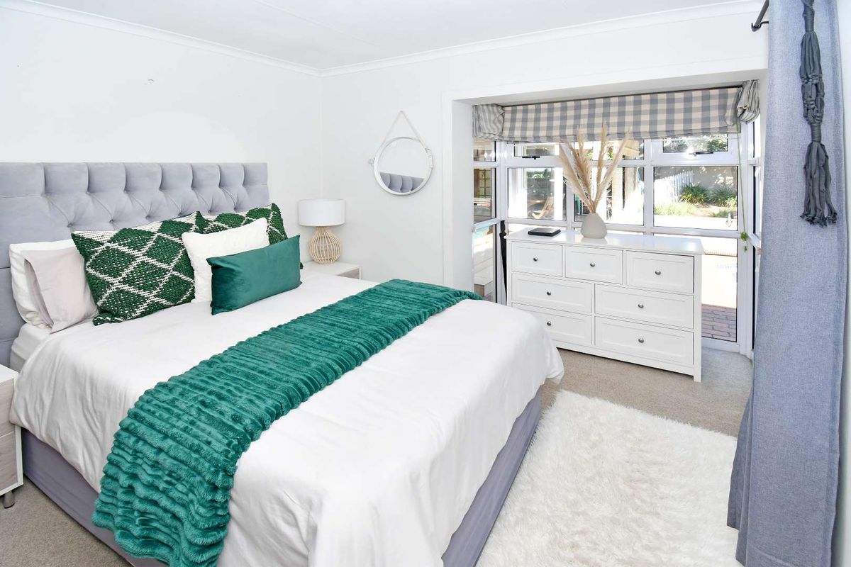A well-maintained bedroom featuring neutral walls, carpeted flooring, and a large window providing natural light and views of the outdoor area.