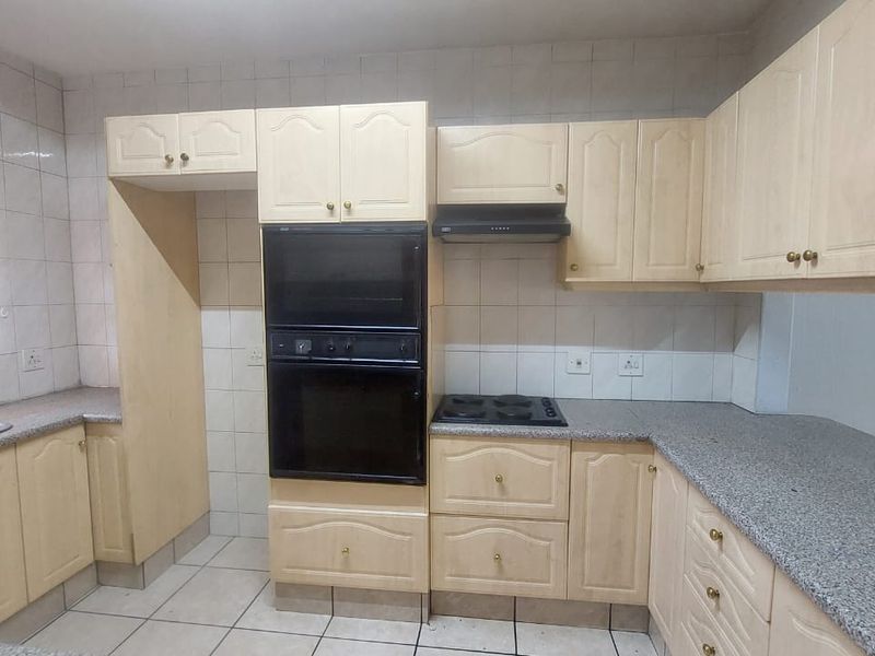 A functional kitchen featuring light-toned built-in cabinetry, granite countertops, a double wall oven, and an electric hob with an extractor fan.