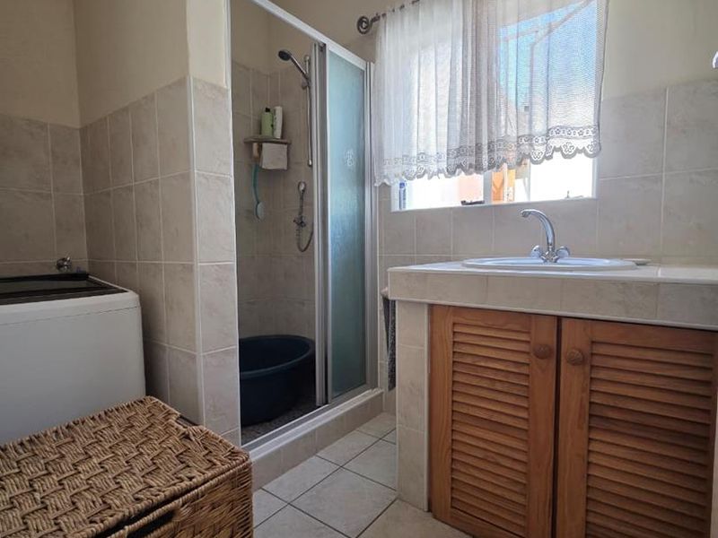A functional bathroom featuring a shower enclosure, tiled vanity with a drop-in basin, and louvered wooden cabinetry.