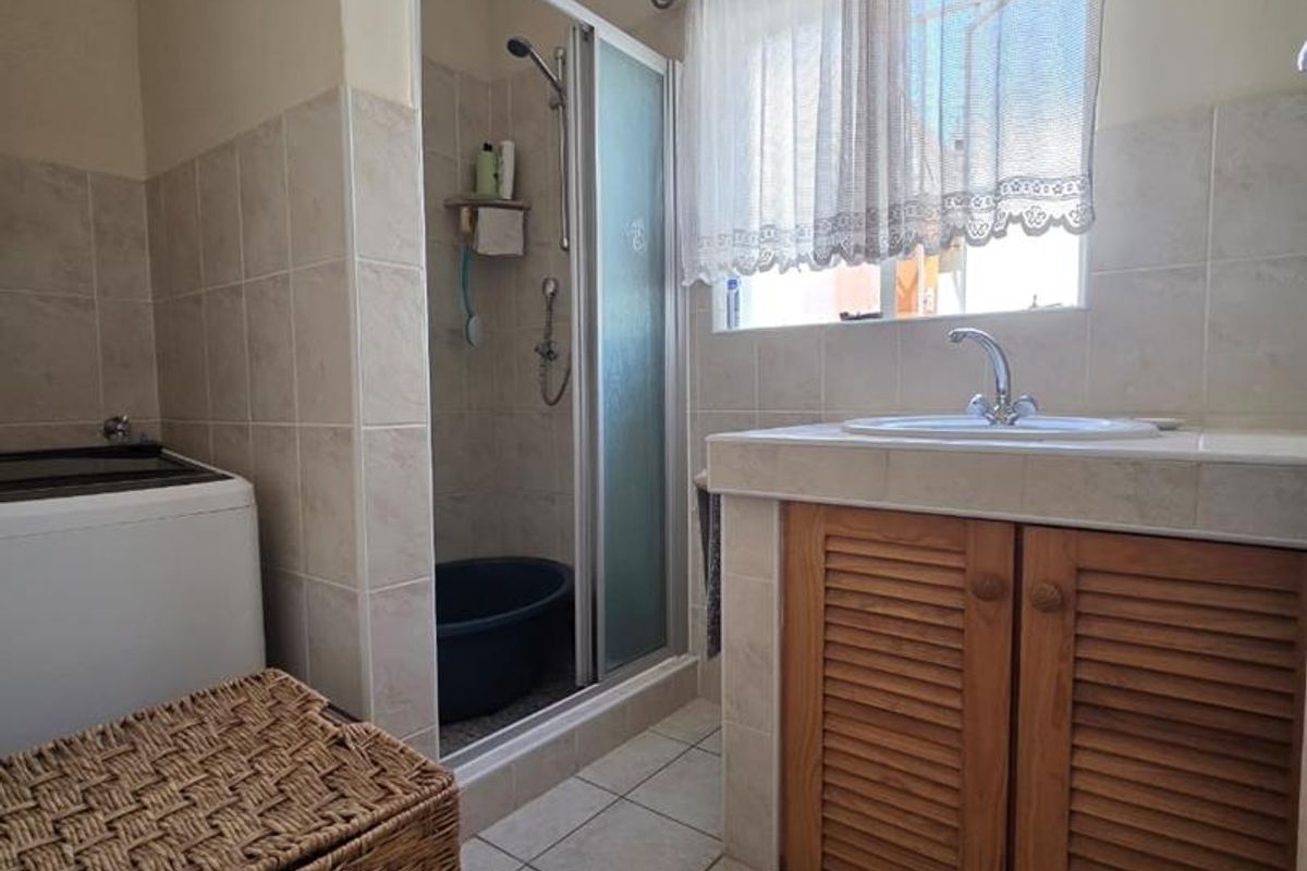 A functional bathroom featuring a shower enclosure, tiled vanity with a drop-in basin, and louvered wooden cabinetry.