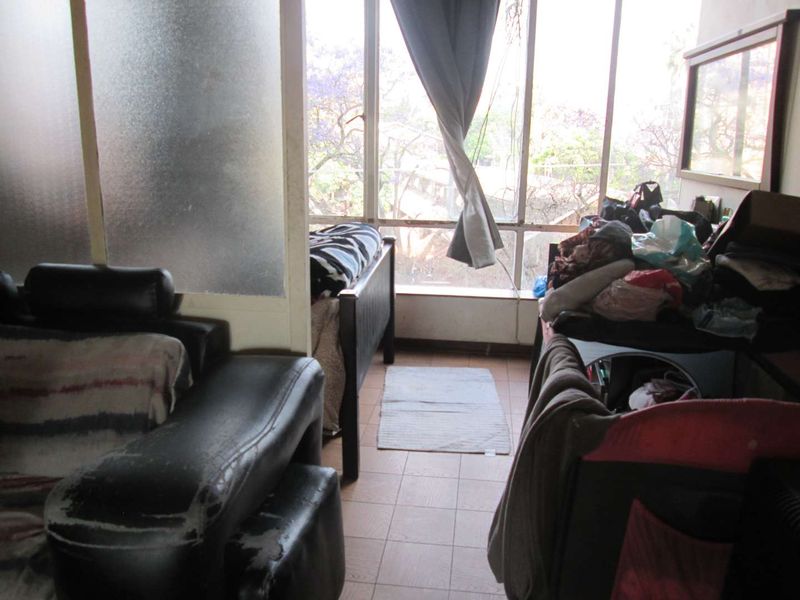A bedroom featuring tiled flooring, a large window providing natural light, and a frosted glass partition separating the space.