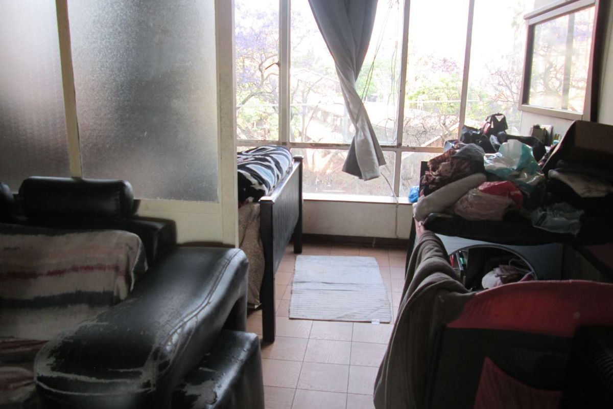 A bedroom featuring tiled flooring, a large window providing natural light, and a frosted glass partition separating the space.