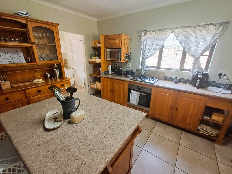 A functional kitchen featuring wooden cabinetry, stone-look countertops, a gas hob, built-in oven, and tiled flooring with a central island workspace.
