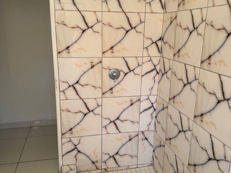 A functional shower enclosure featuring decorative marble-effect wall tiles and a mosaic tiled floor base.