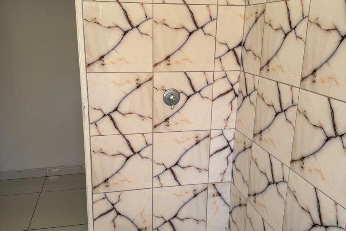 A functional shower enclosure featuring decorative marble-effect wall tiles and a mosaic tiled floor base.