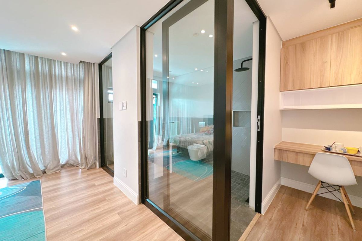 Modern bedroom featuring a sleek glass-enclosed shower, integrated built-in desk with cabinetry, and high-quality laminate flooring in a contemporary design.