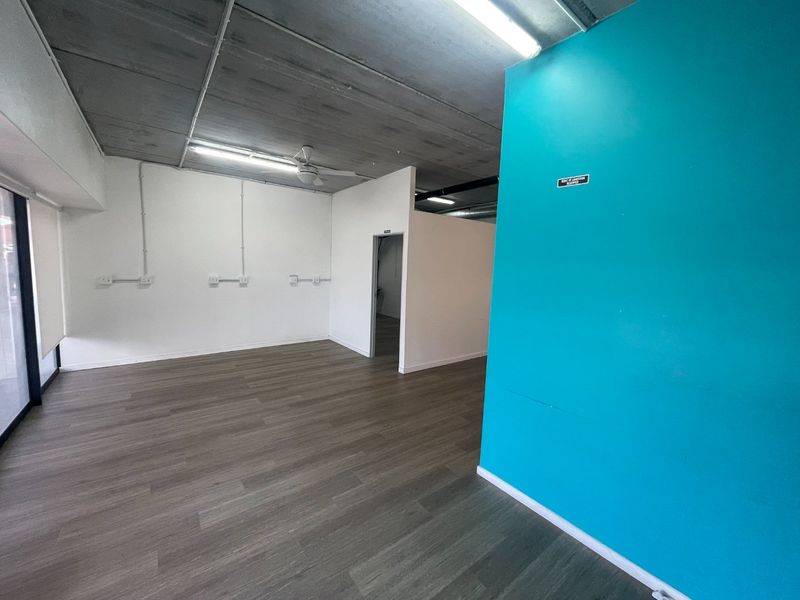 An open-plan retail space featuring exposed concrete ceilings, laminate flooring, and surface-mounted electrical conduits, offering a versatile layout for various business needs.