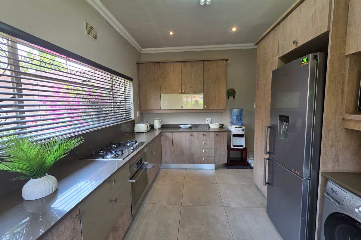 Modern kitchen featuring wood-look cabinetry, stone countertops, a built-in gas hob, under-counter oven, and tiled flooring.