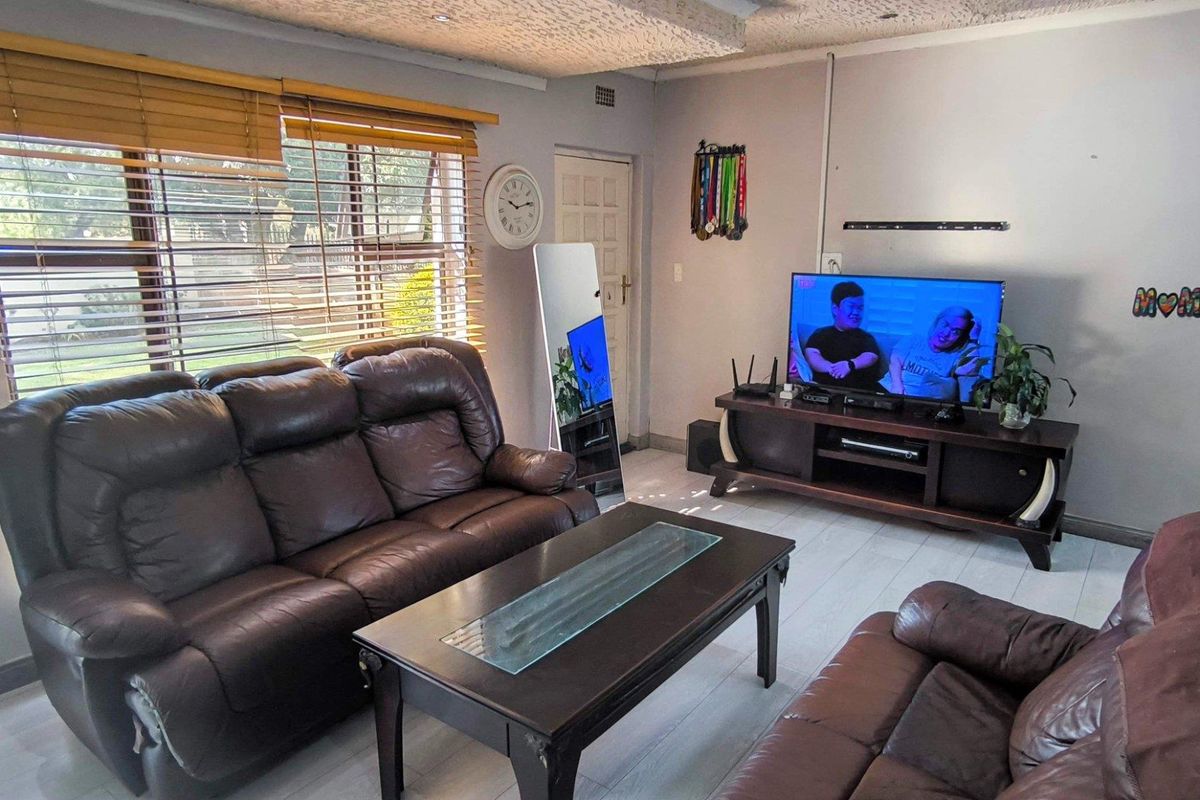 A living room featuring light-toned flooring, large windows with wooden blinds, and a textured ceiling finish.