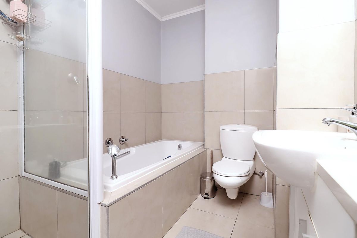 A clean, functional bathroom featuring a built-in bathtub with shower screen, a wall-mounted toilet, and a modern vanity basin with neutral wall tiling.
