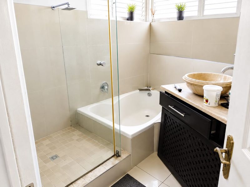 A functional bathroom featuring a built-in bathtub, glass-enclosed shower, and a stone-topped vanity with a vessel sink.