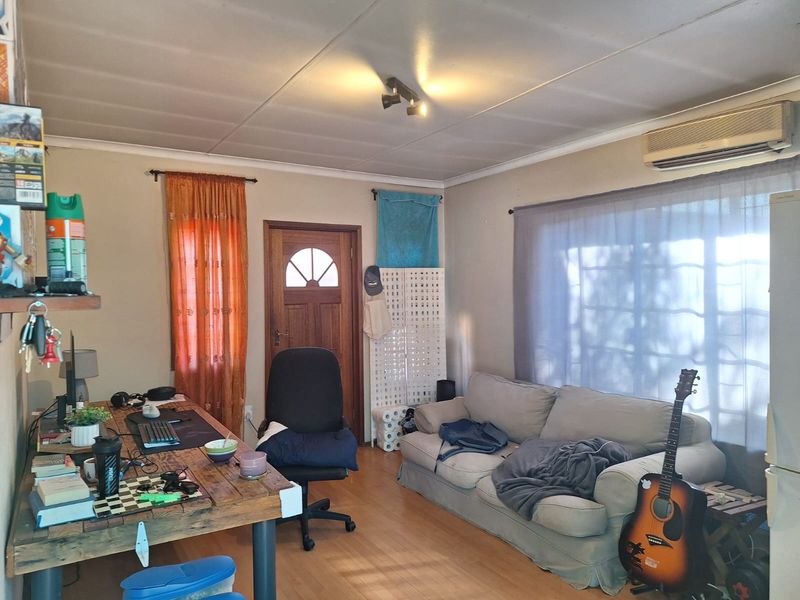 A living room featuring laminate flooring, a timber entrance door, and a wall-mounted split-system air conditioning unit.