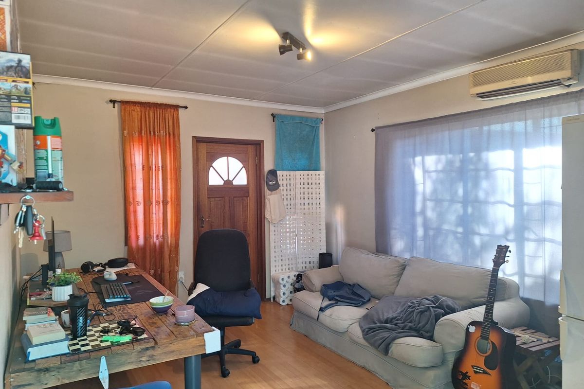 A living room featuring laminate flooring, a timber entrance door, and a wall-mounted split-system air conditioning unit.