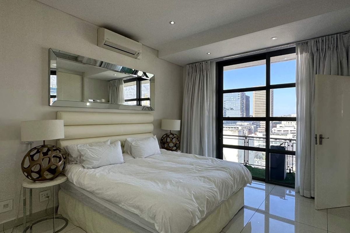 Modern bedroom featuring large floor-to-ceiling windows with city views, tiled flooring, recessed ceiling lighting, and a wall-mounted air conditioning unit.