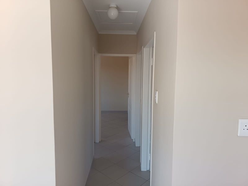 A clean, neutral-toned hallway featuring tiled flooring and a ceiling access hatch, providing a bright and functional transition space between rooms.