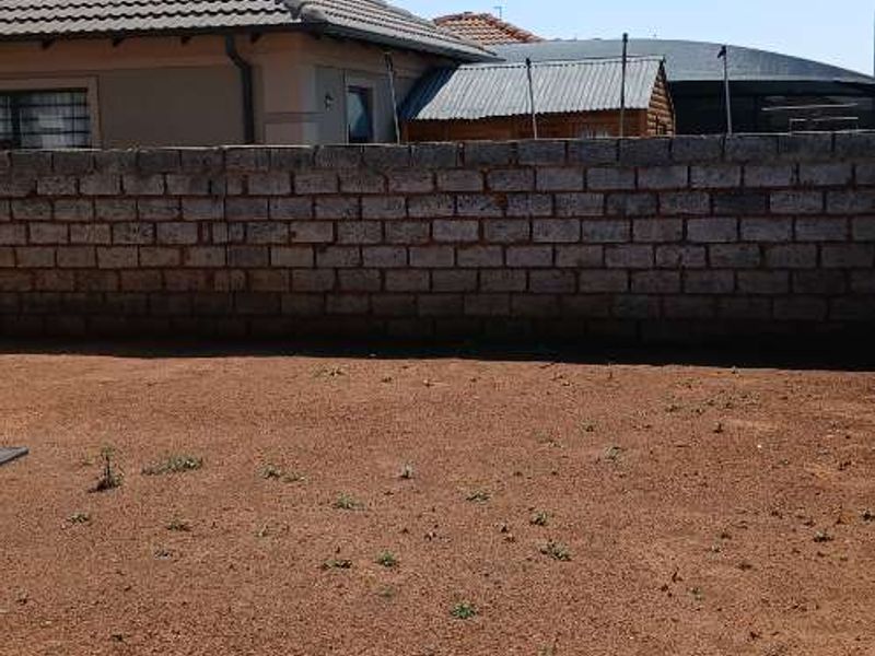 A rear exterior view of the property featuring a brick boundary wall with security spikes and an unlandscaped garden area.