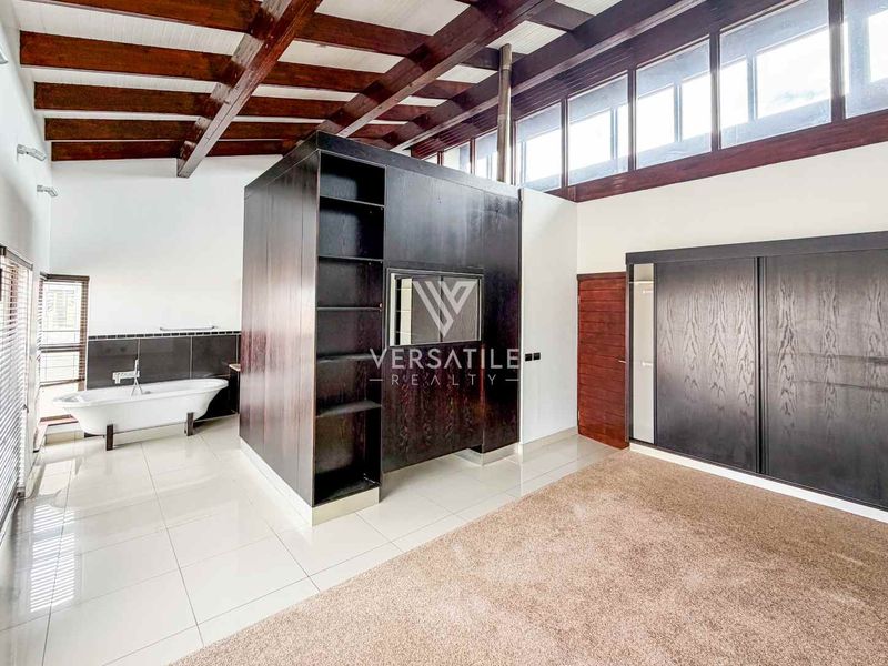 Spacious bedroom featuring exposed timber beams, clerestory windows, built-in cupboards, and an integrated open-plan freestanding bathtub area.