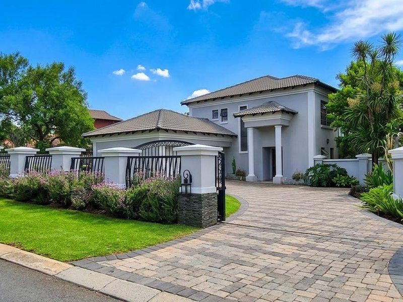 A well-maintained double-story residence featuring a paved driveway, stone-clad entrance pillars, and manicured garden landscaping with secure wrought iron fencing.