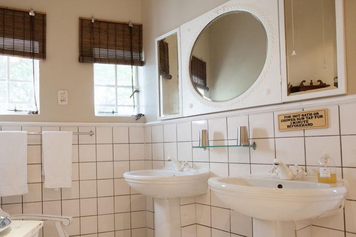 A classic bathroom featuring dual pedestal sinks, white wall tiling, and a large decorative mirror with integrated cabinetry.