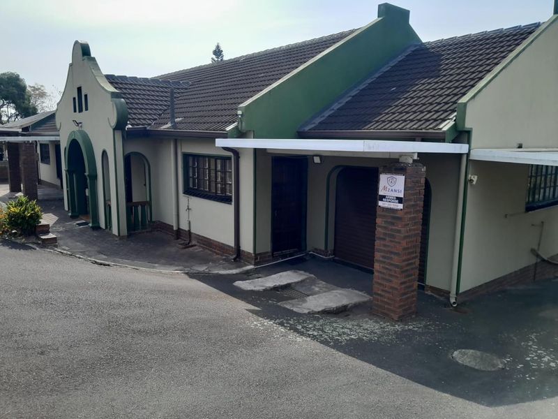 Front elevation of a house featuring a tiled roof, brick pillar, and garage access with a paved driveway.