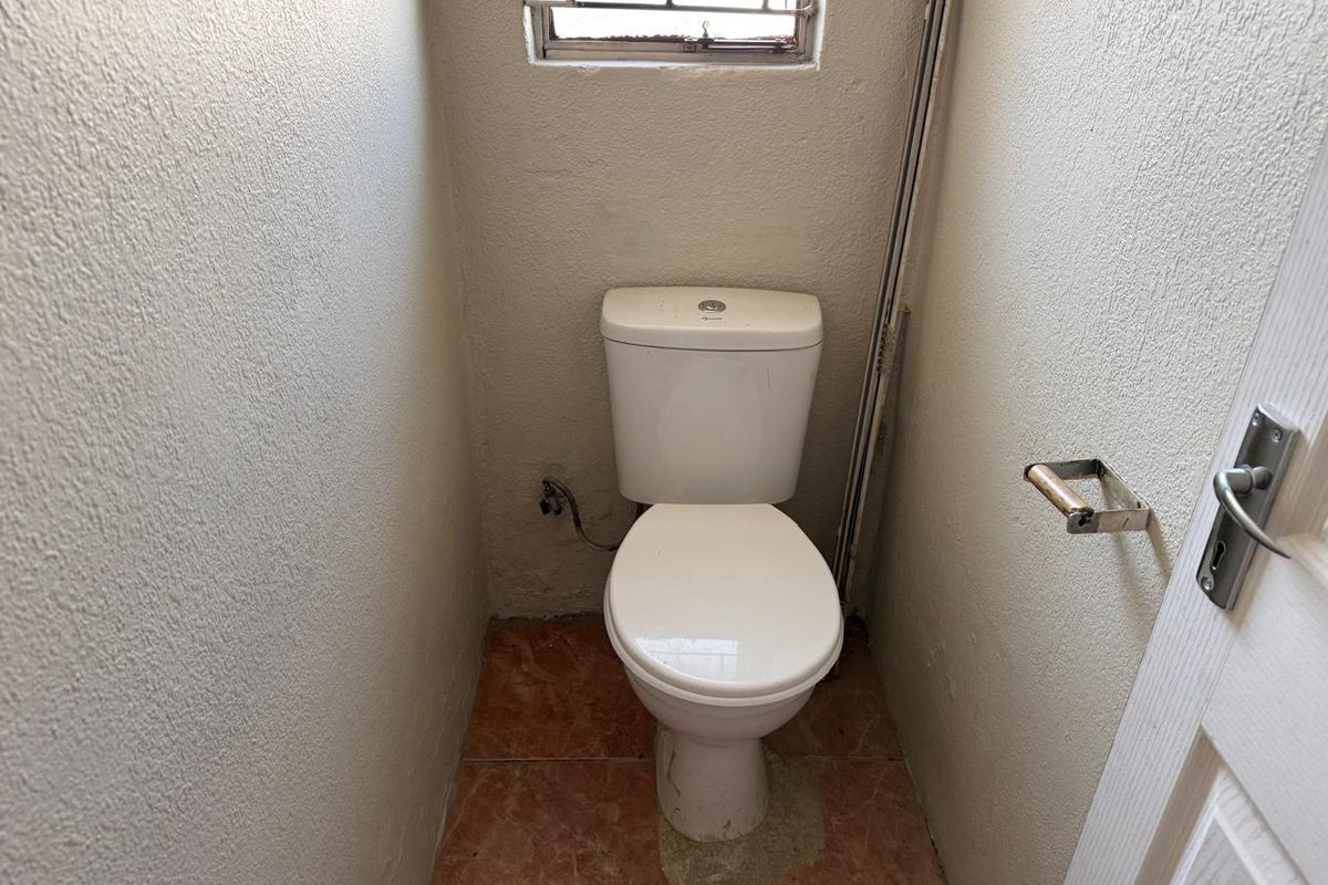 A compact guest toilet featuring tiled flooring, a standard white toilet suite, and a security window grille.