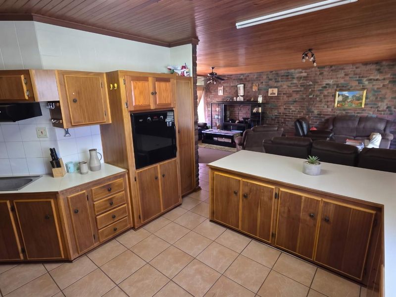 Open-plan kitchen and living area featuring timber ceilings, exposed brick walls, ceramic tile flooring, and traditional wooden cabinetry with integrated oven and extractor fan.
