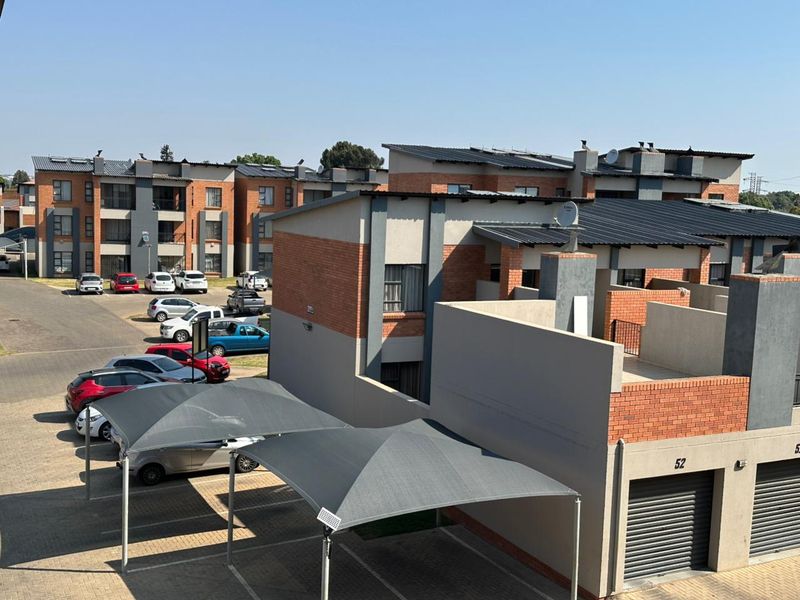 Exterior view of a modern apartment complex featuring brick and plaster facades, metal roofing, and covered parking bays.