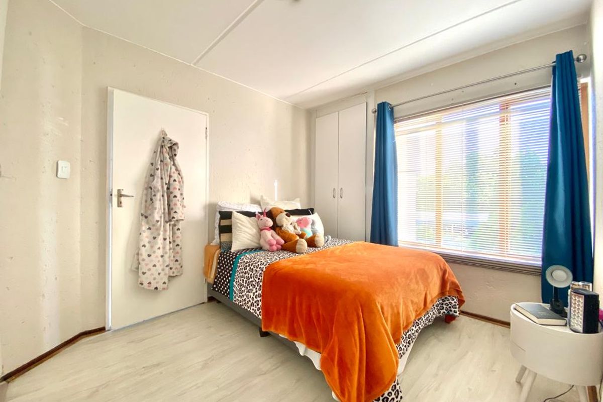 A bedroom featuring built-in cupboards, light-toned laminate flooring, and a large window with blinds, providing a functional and well-lit living space.