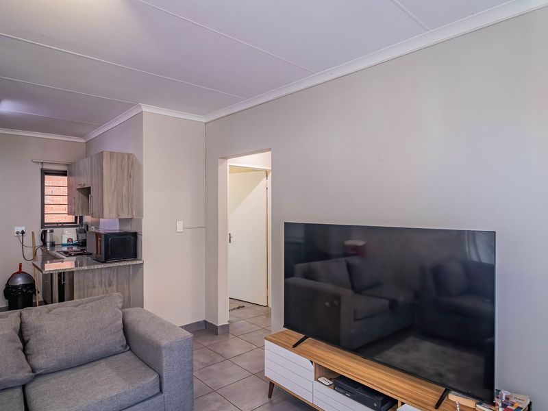 Open plan living area featuring tiled floors, a compact kitchen with built-in cabinetry, and direct access to an internal hallway.