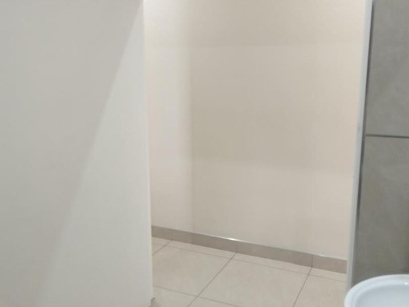 A clean, modern bathroom space featuring neutral floor and wall tiling, recessed lighting, and a minimalist washbasin.