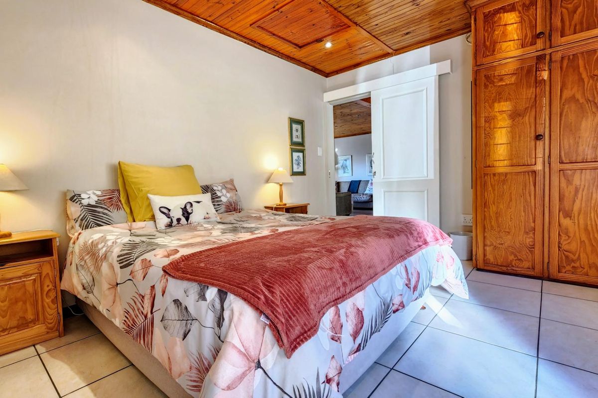 A bedroom featuring a wooden panelled ceiling, built-in wooden wardrobe, and tiled flooring, with a sliding door leading to an adjacent living space.