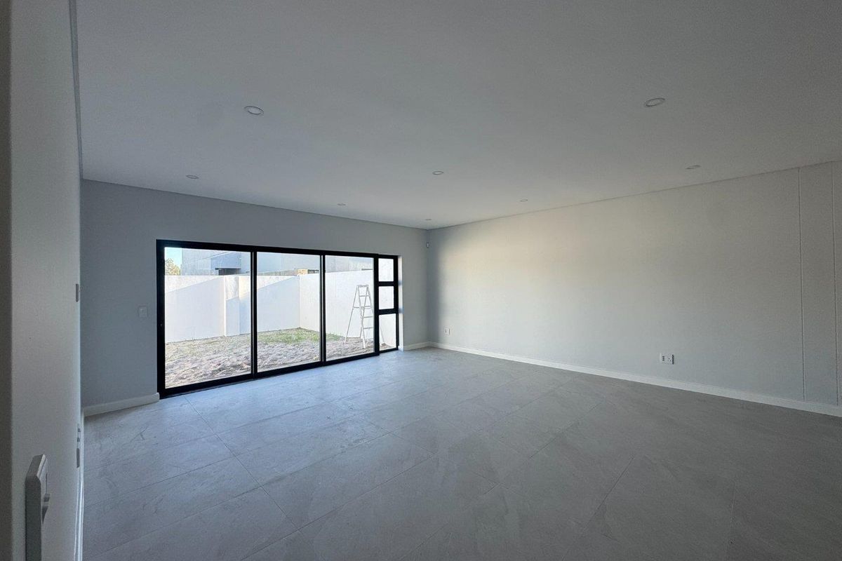 A spacious, empty living area featuring large black-framed sliding glass doors that open to a private rear garden.