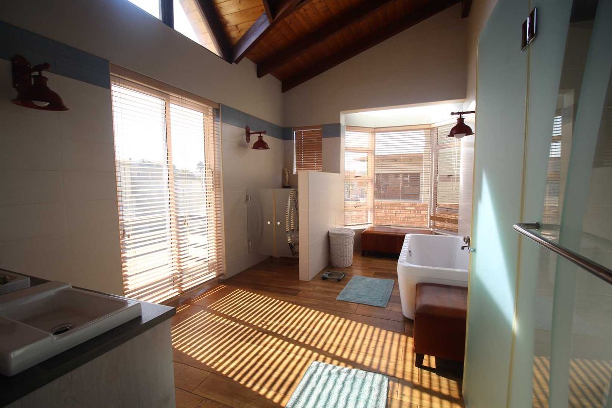 Spacious bathroom featuring a freestanding bathtub, vanity basin, and high vaulted timber ceilings with abundant natural light from large windows and sliding doors.