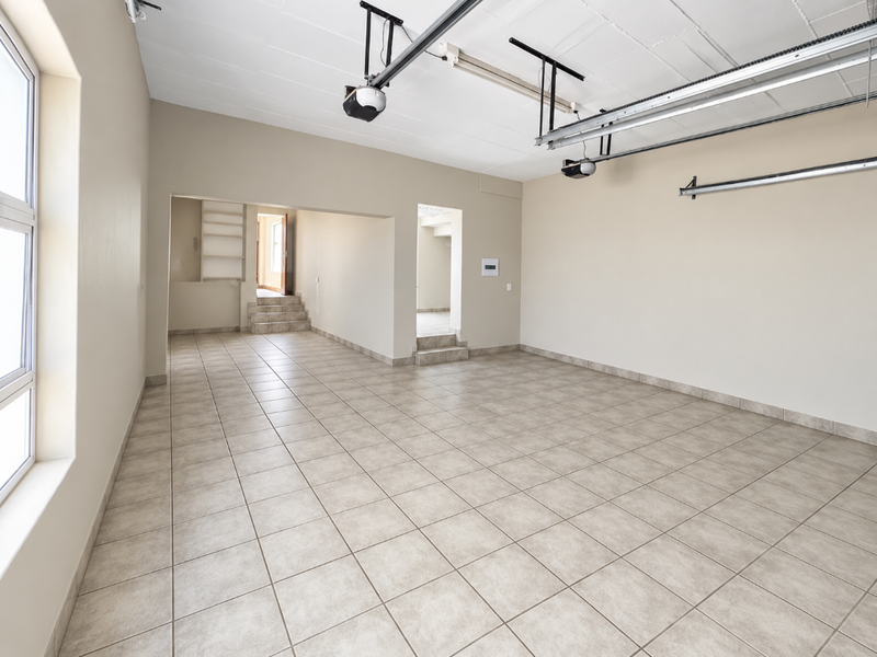 Spacious, clean garage featuring tiled flooring, automatic door mechanisms, and convenient built-in shelving with stepped access to the interior.