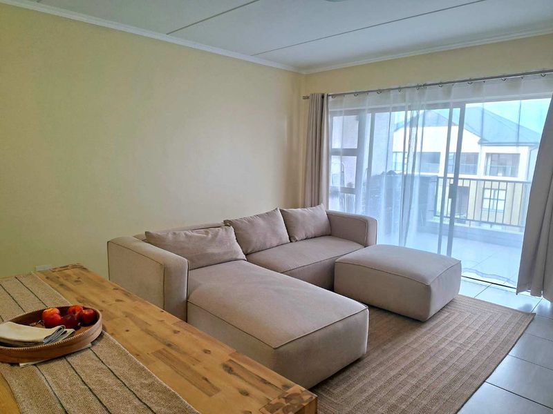 A bright living room featuring tiled flooring and a large sliding glass door that provides access to an outdoor balcony area.