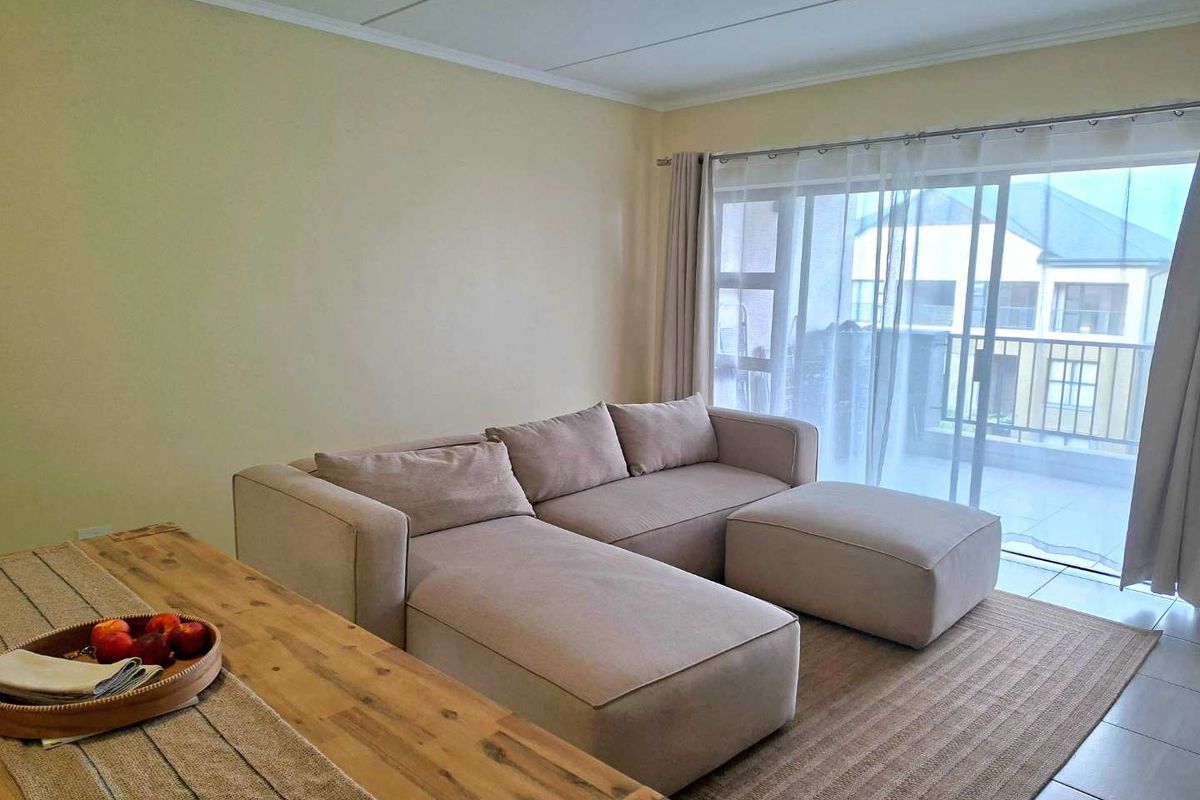A bright living room featuring tiled flooring and a large sliding glass door that provides access to an outdoor balcony area.