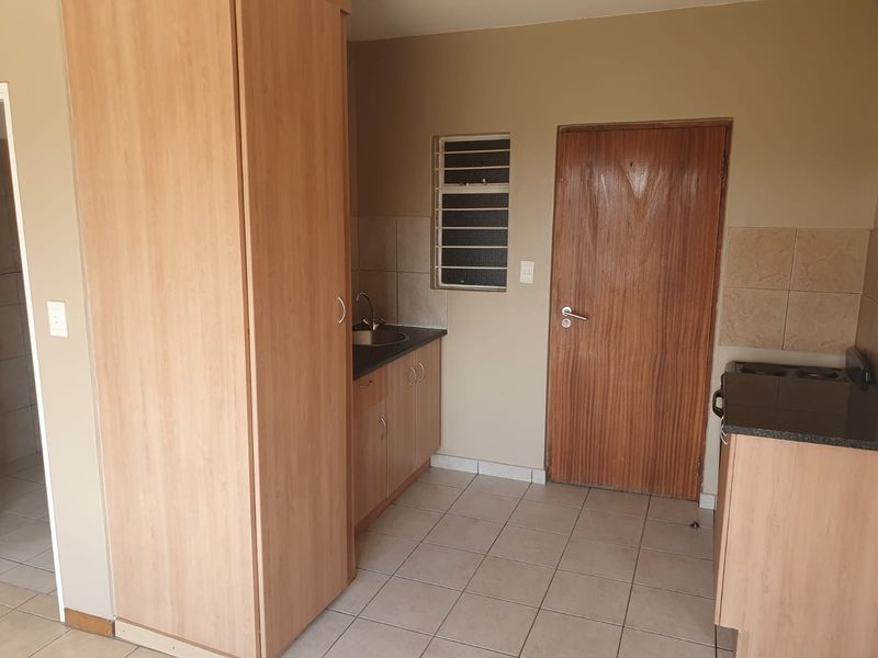 A compact kitchen area featuring built-in cabinetry, laminate countertops, a stainless steel sink, and tiled flooring, offering a functional space for culinary activities.