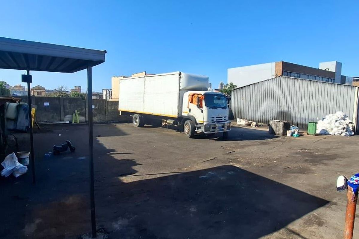 An industrial rear yard featuring an asphalt surface, a metal storage shed, and a covered loading area, suitable for commercial or logistics operations.