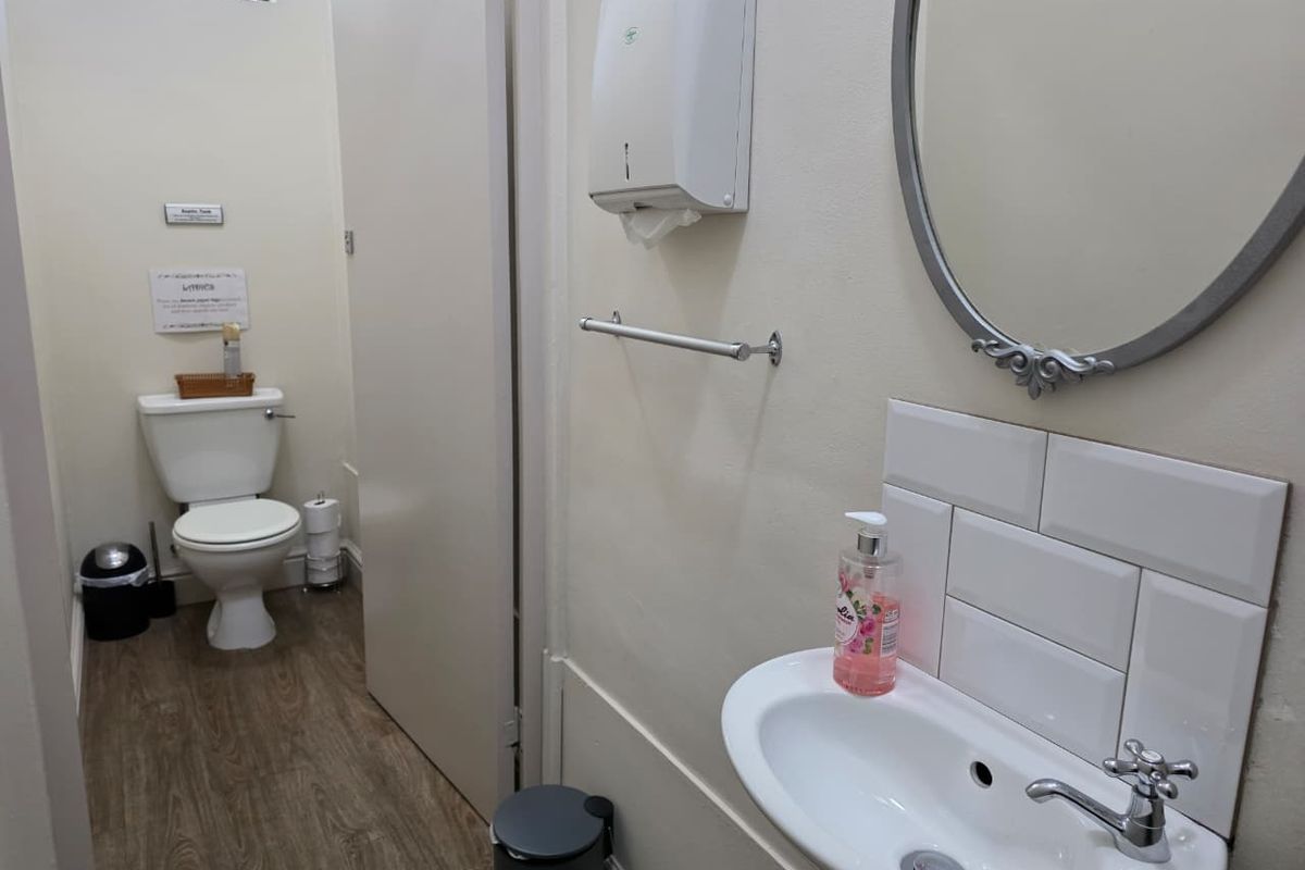 A functional bathroom featuring a toilet, wall-mounted washbasin with a tiled splashback, and essential fixtures including a towel rail and paper towel dispenser.