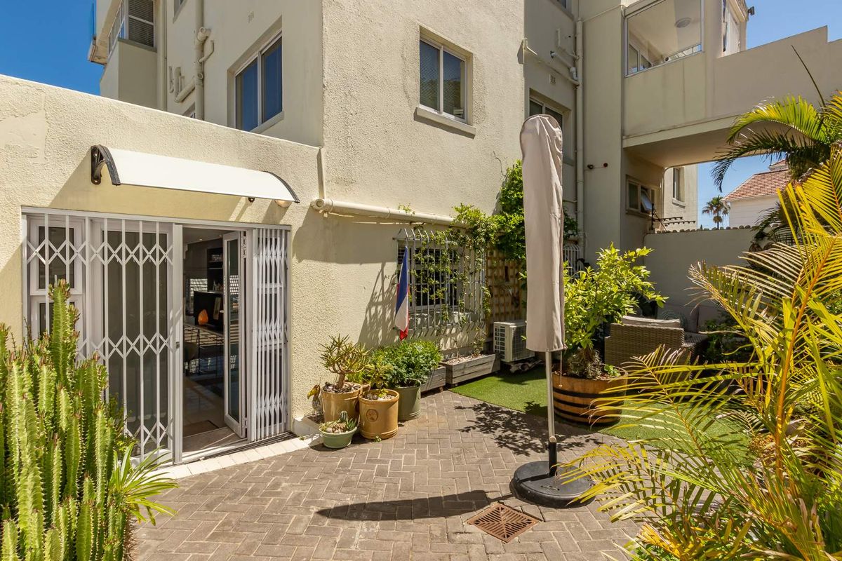 A private rear courtyard featuring brick paving, artificial lawn, and secure metal security gates leading into the apartment interior.