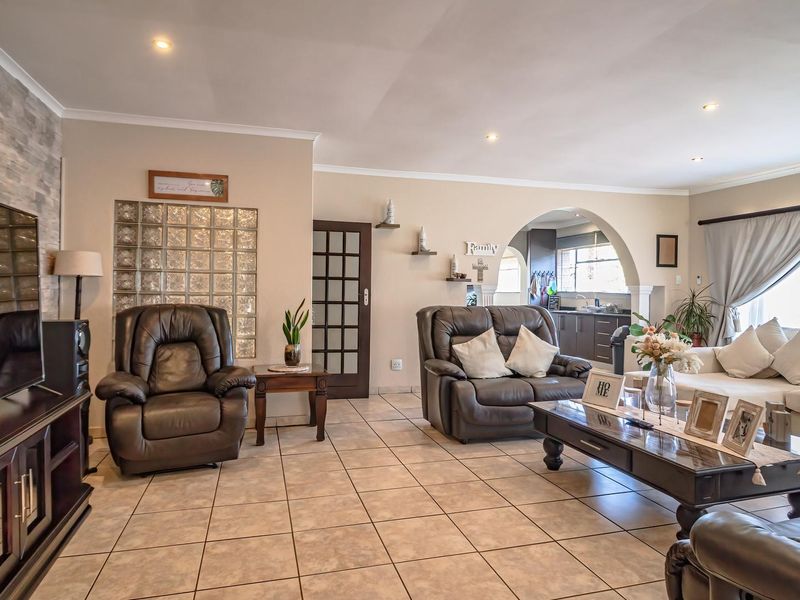 Spacious open-plan living area featuring tiled flooring, a decorative glass block wall, stone veneer accent, and an arched transition to the kitchen area.