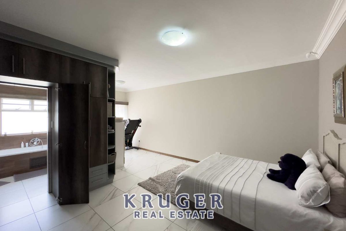 Spacious bedroom featuring large format floor tiles, built-in dark wood cabinetry, and an integrated en-suite bathroom area.