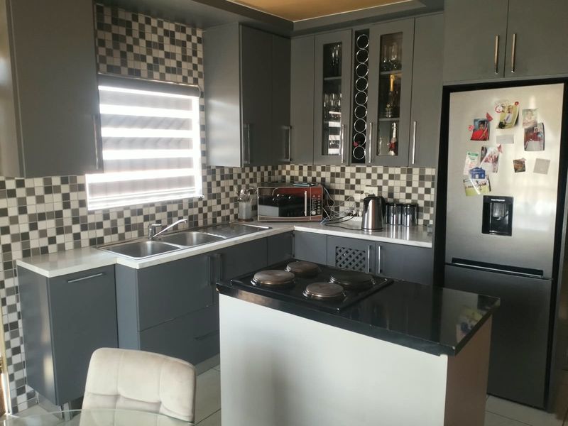 Modern kitchen featuring dark grey cabinetry, contrasting stone countertops, a tiled checkerboard backsplash, and a central island with an integrated electric hob.