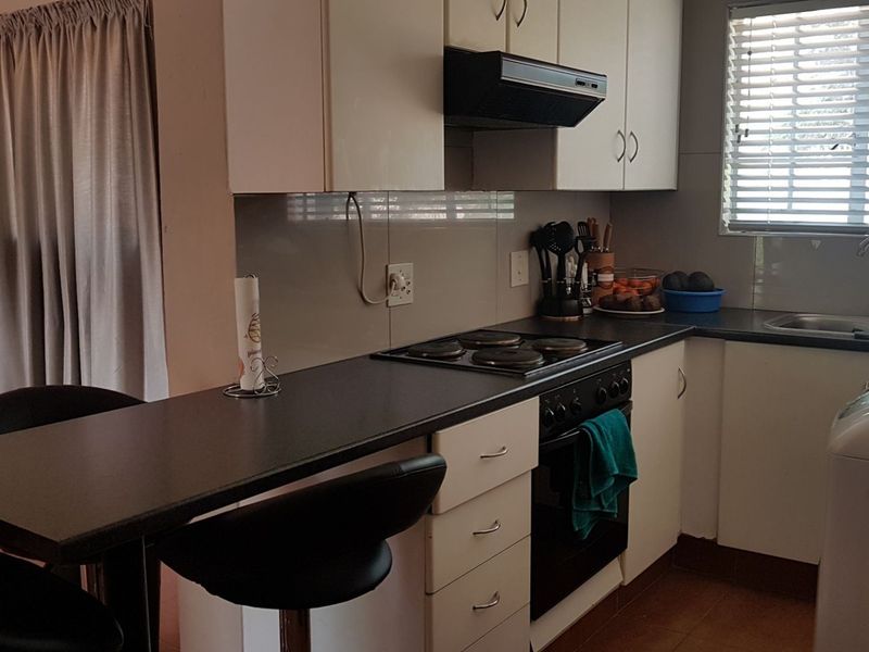 A functional kitchen featuring white cabinetry, dark laminate countertops, an integrated electric hob, oven, extractor fan, and a convenient breakfast bar area.
