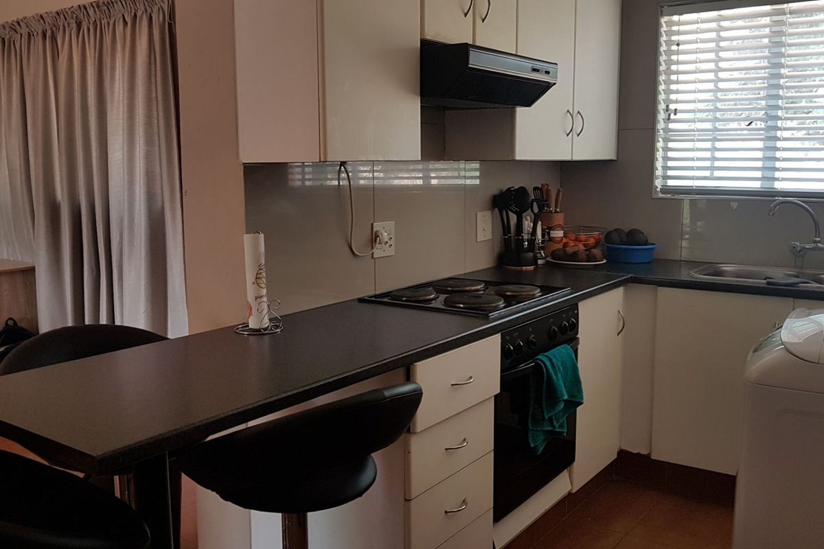 A functional kitchen featuring white cabinetry, dark laminate countertops, an integrated electric hob, oven, extractor fan, and a convenient breakfast bar area.