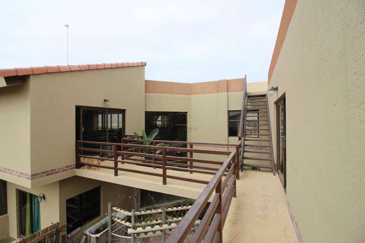 An elevated exterior walkway connecting sections of the house, featuring timber balustrades, tiled flooring, and an external staircase leading to the upper level.