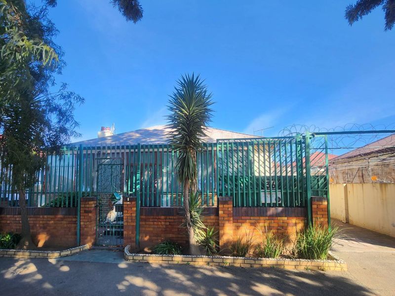 Front exterior view of the property featuring a brick boundary wall, metal security fencing with razor wire, and a paved driveway entrance.