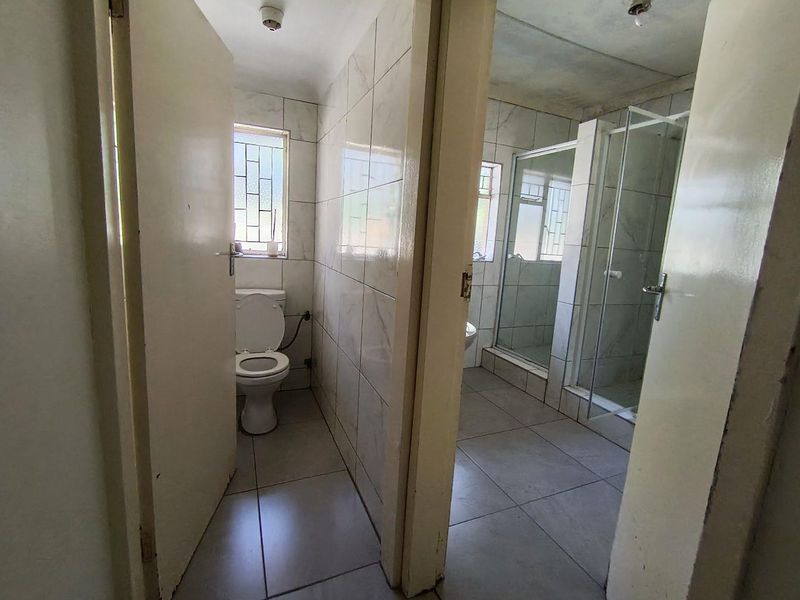 A functional bathroom featuring a separate toilet area and a glass-enclosed shower with neutral wall and floor tiling.